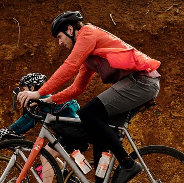 two cyclists ride past a dirt wall
